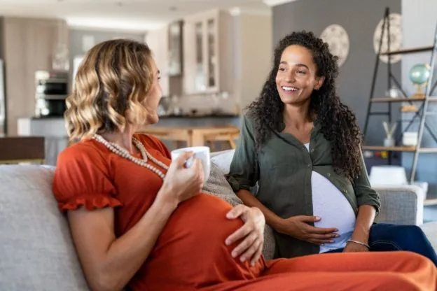 Two pregnant women talking together on a sofa